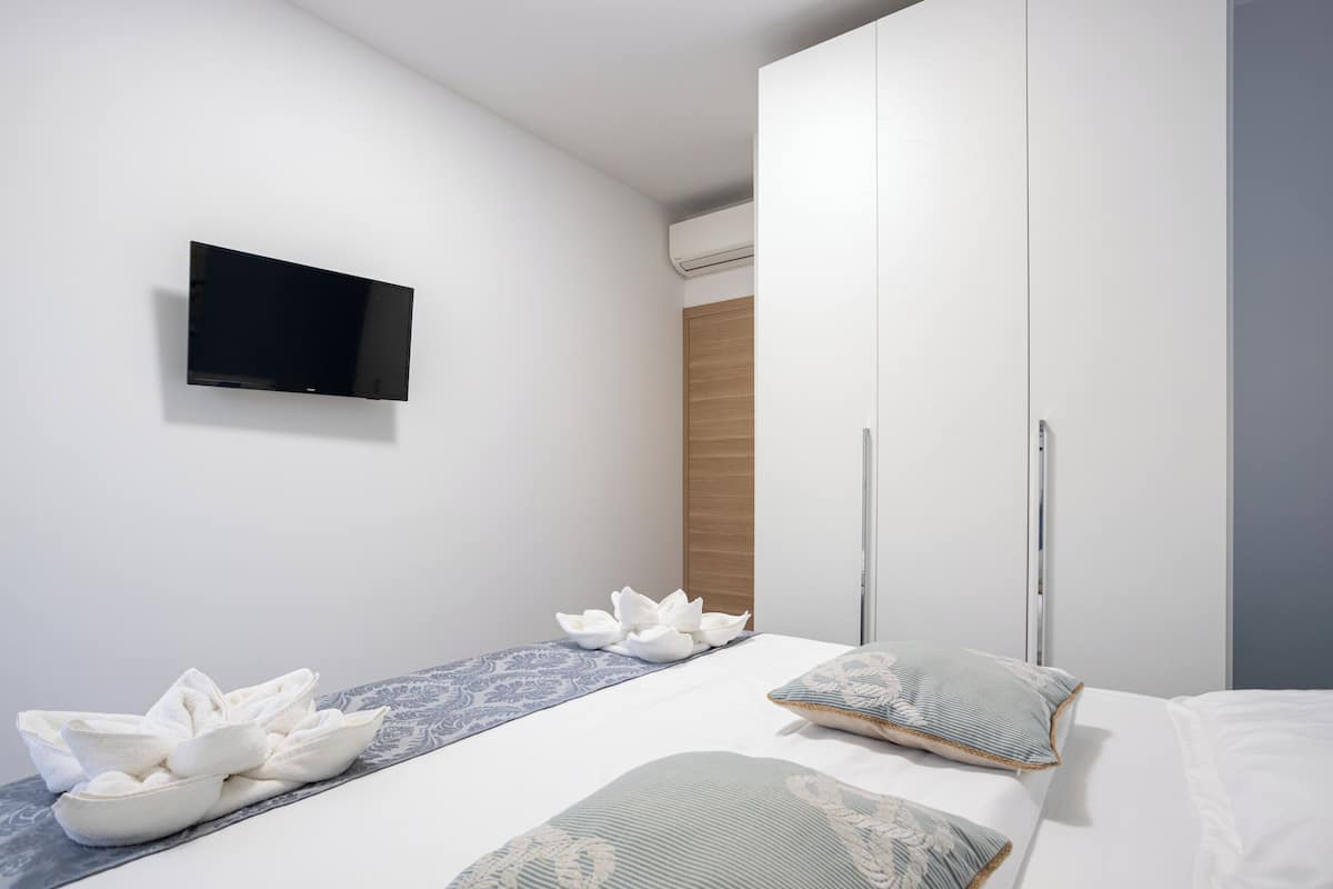 A modern bedroom with a bed, a flat-screen TV mounted on the wall, and a wardrobe with sliding doors.