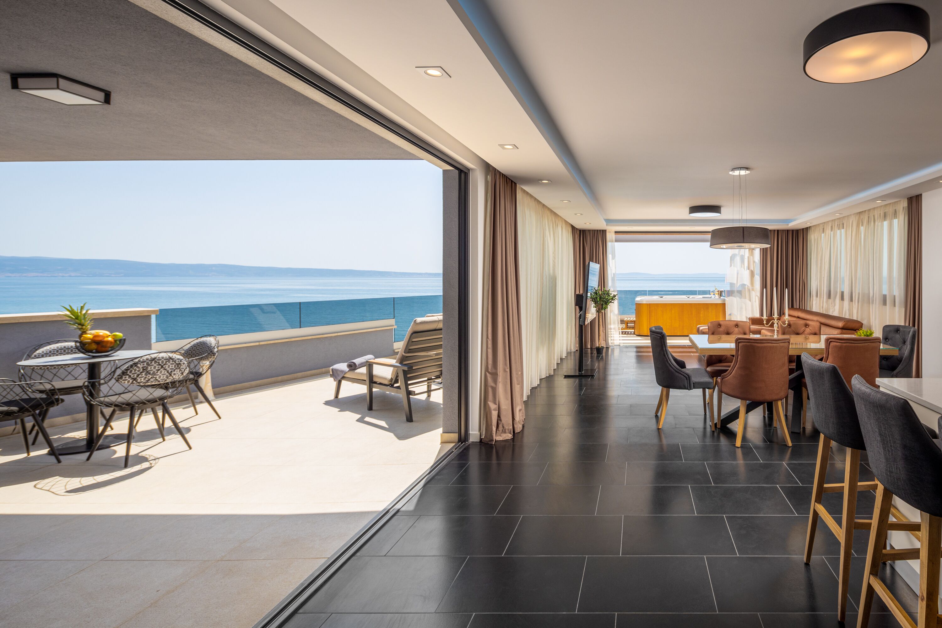 Habitación de hotel moderna con balcón con vistas al mar, zona de comedor con muebles contemporáneos y vista al océano.