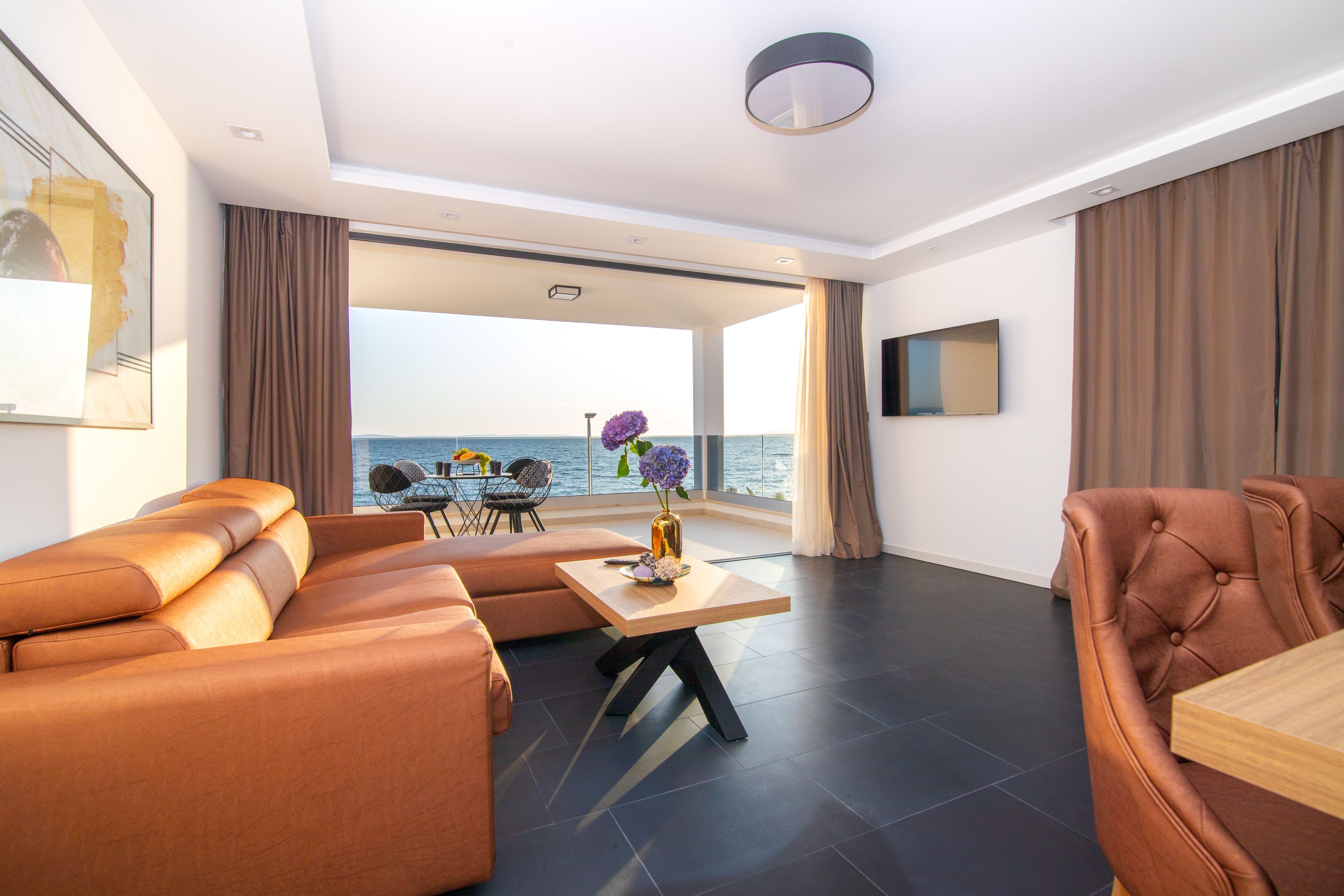 A modern living room with a sofa, a dining table, and a view of the sea.