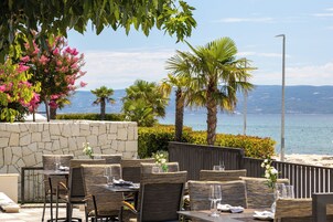 Un comedor al aire libre con mobiliario de mimbre, una pared de piedra y vistas al mar.