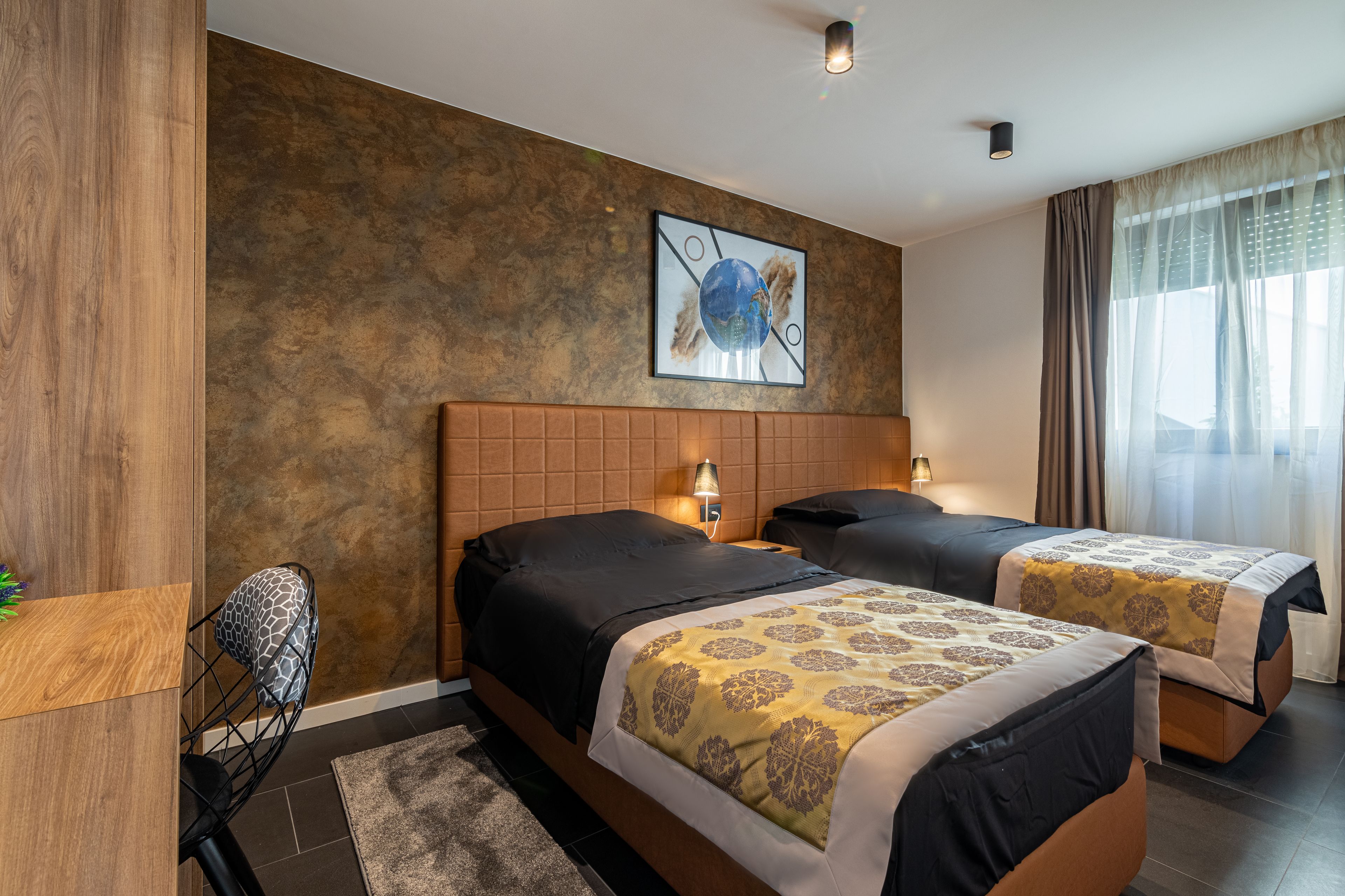 Habitación de hotel con dos camas, un cabecero de madera, un cuadro con forma de globo terráqueo y una ventana con cortinas.