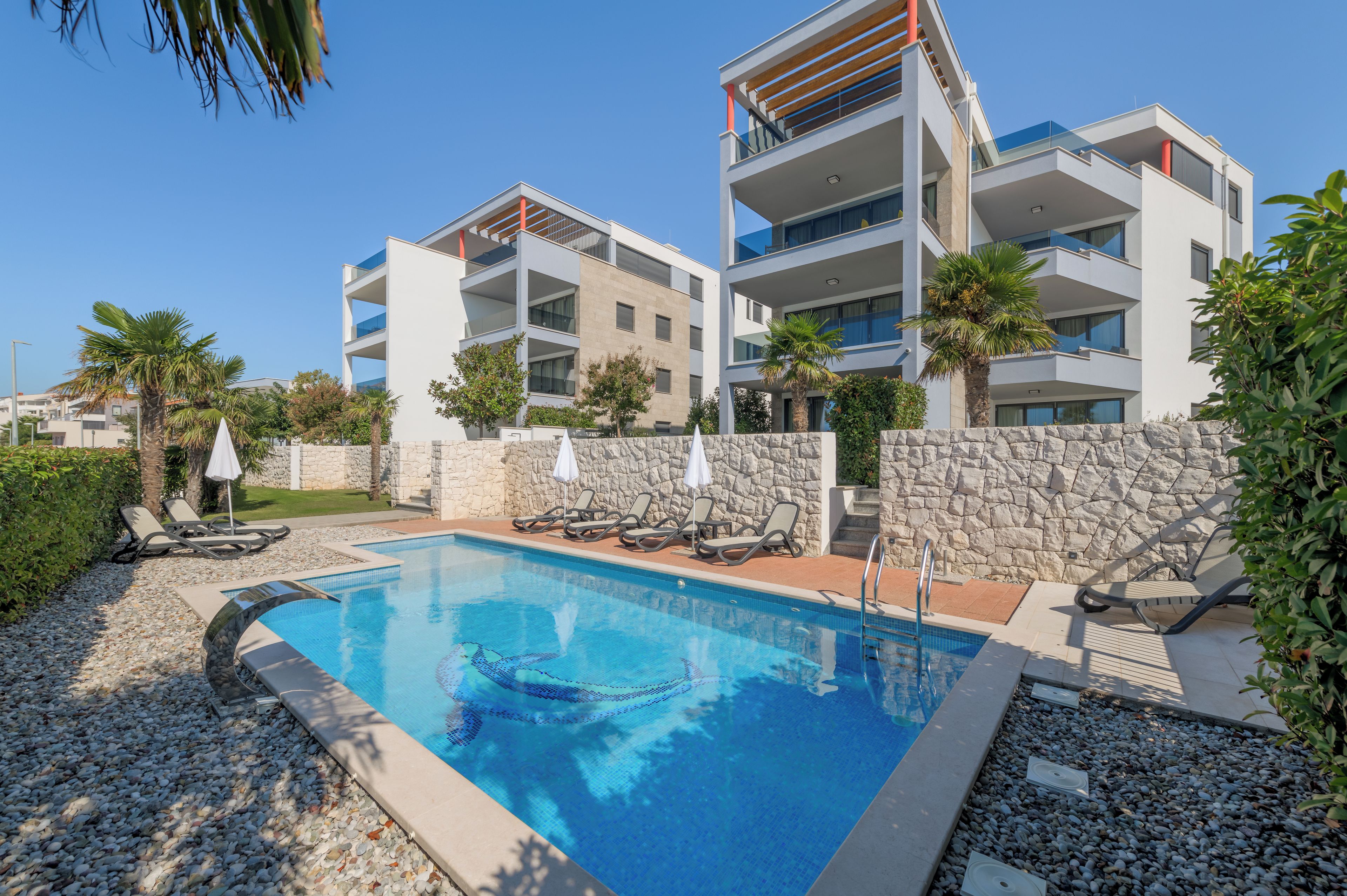 A modern hotel with a swimming pool, lounge chairs, and a stone wall.