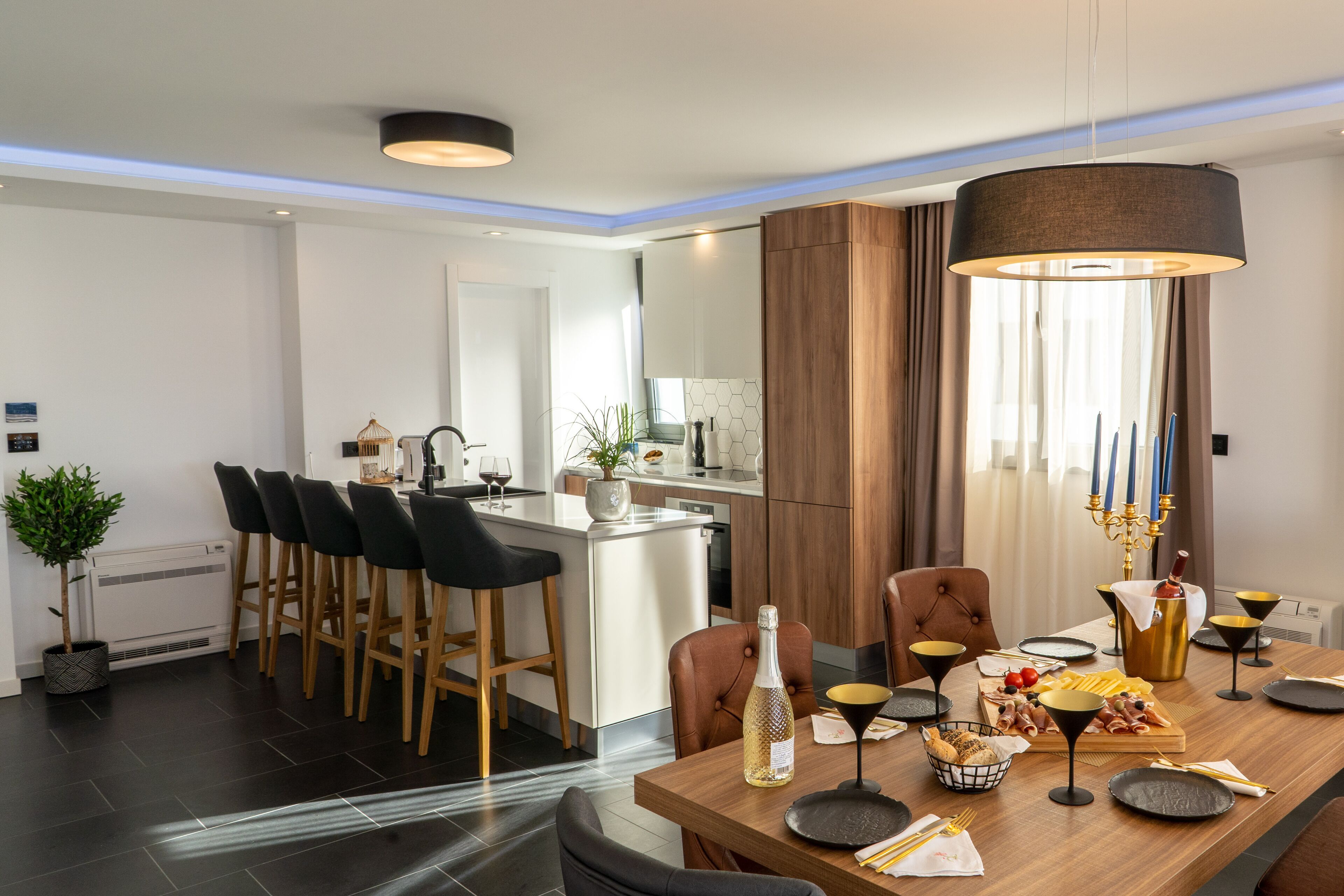 A modern kitchen with a central island, bar stools, and a dining table set for a meal.