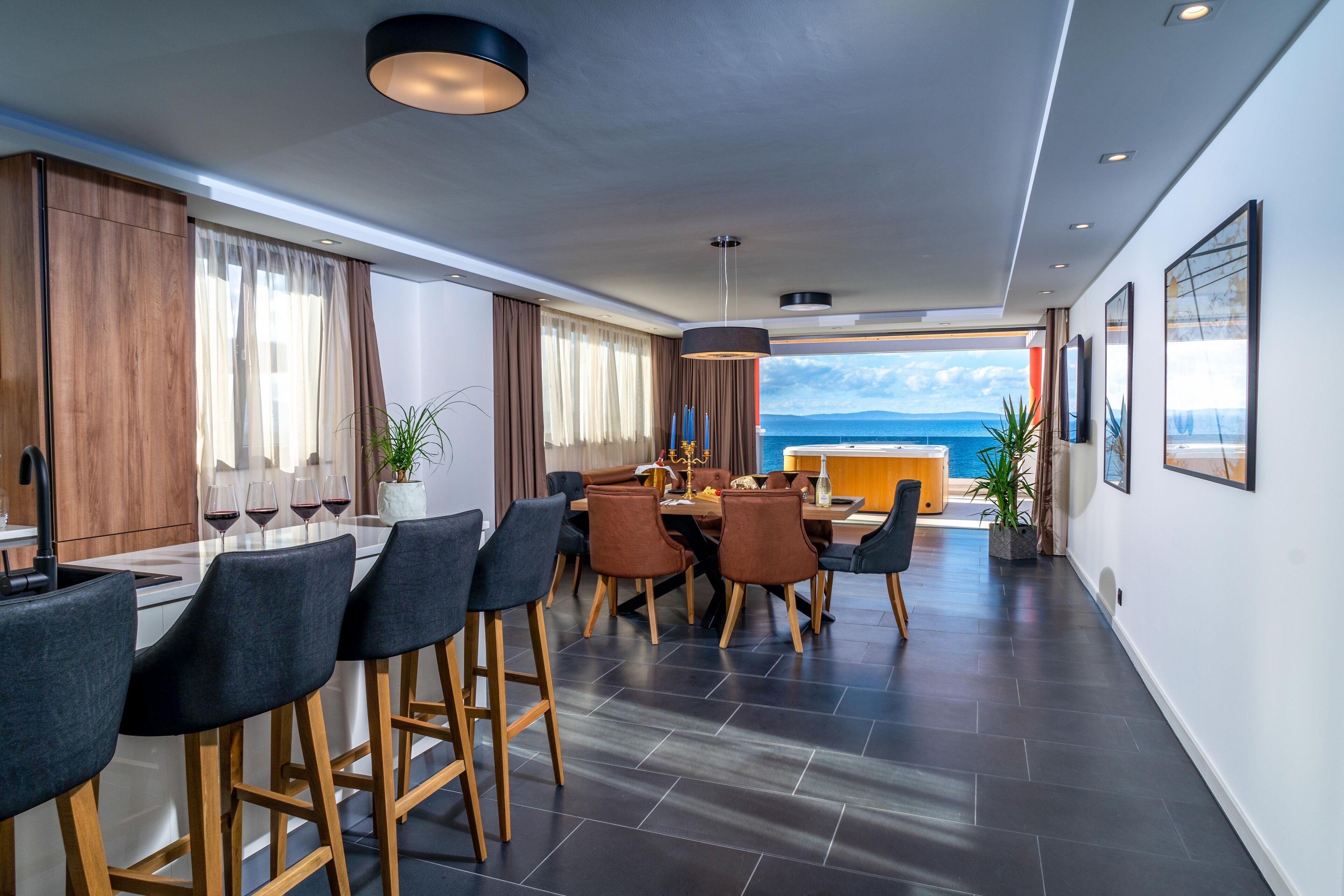A modern kitchen with a dining area, large windows, and a view of the sea.
