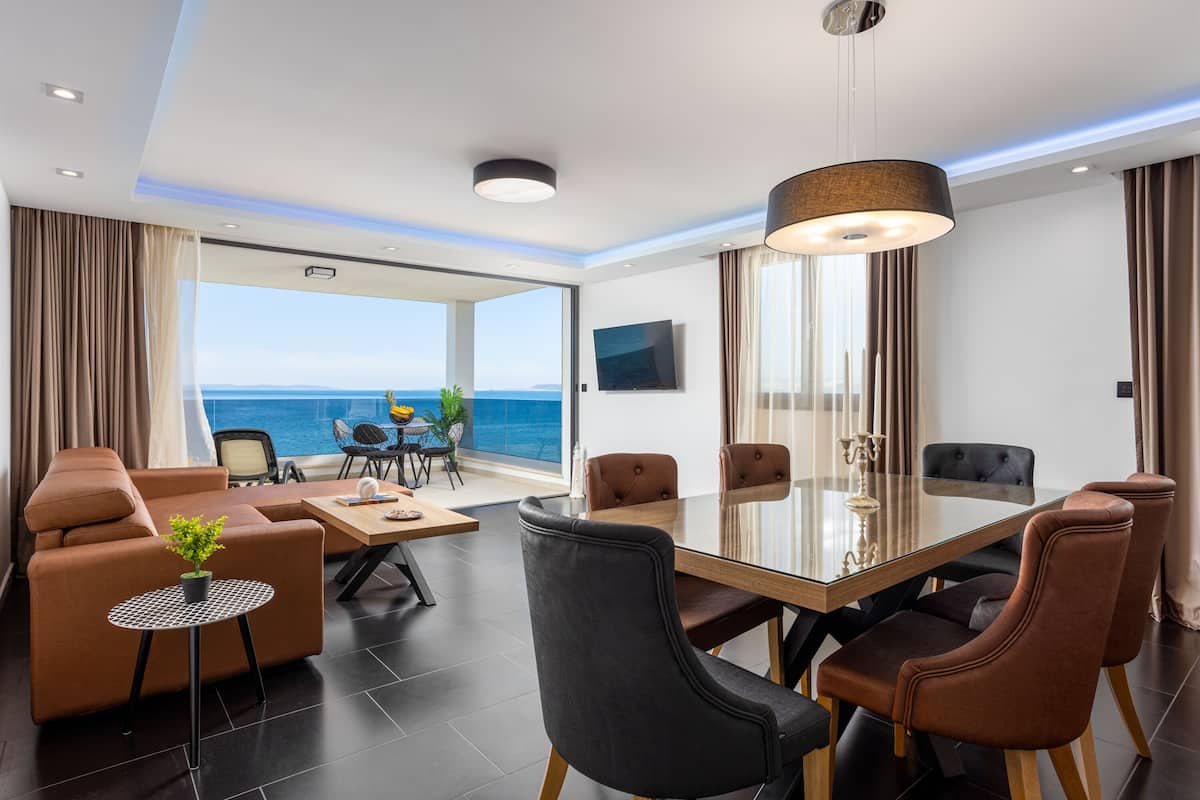 A modern hotel room with a large glass table, comfortable seating, and a view of the sea.