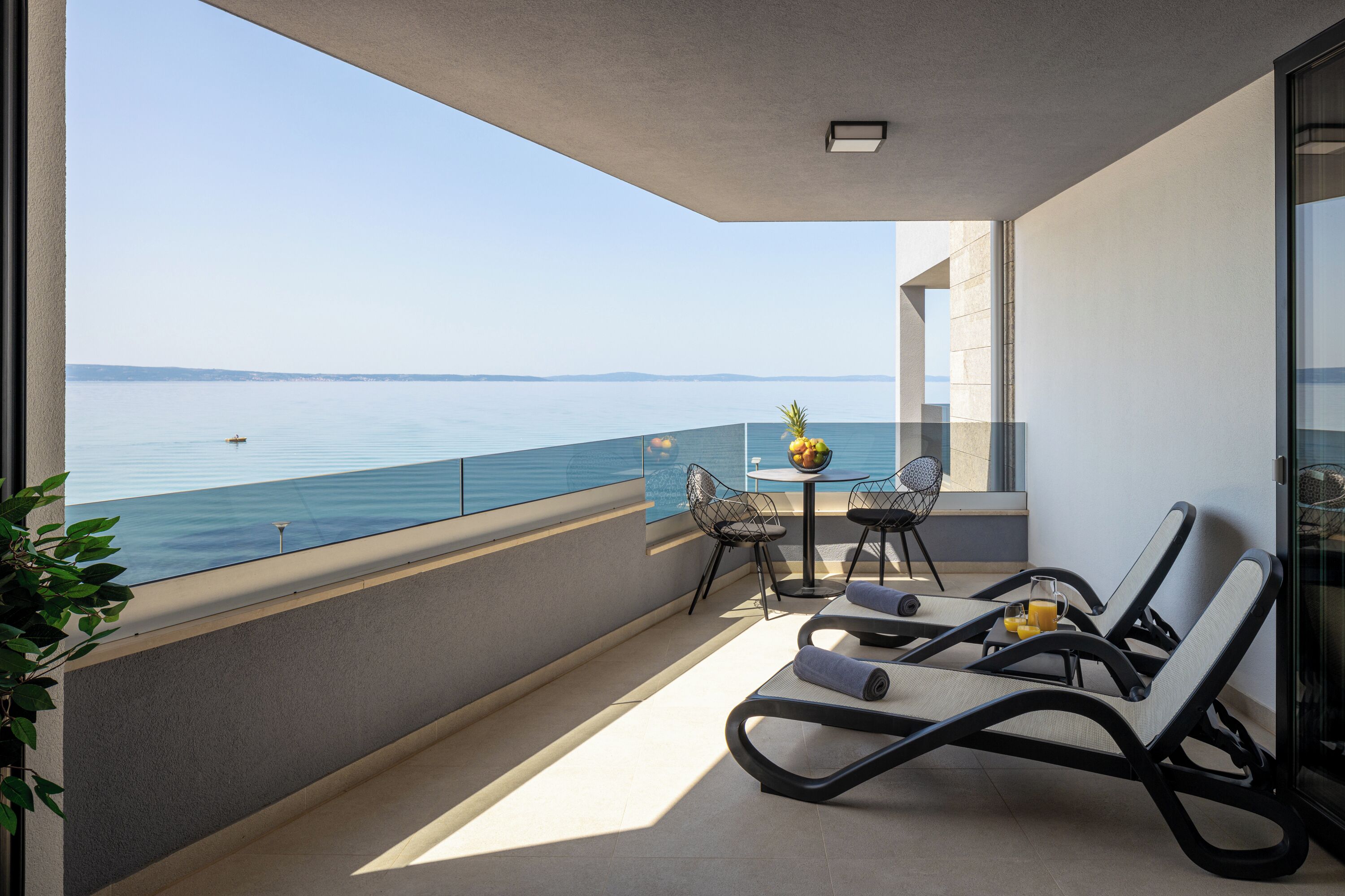 Un balcón con vista al mar, una mesa con sillas y sillones de descanso.