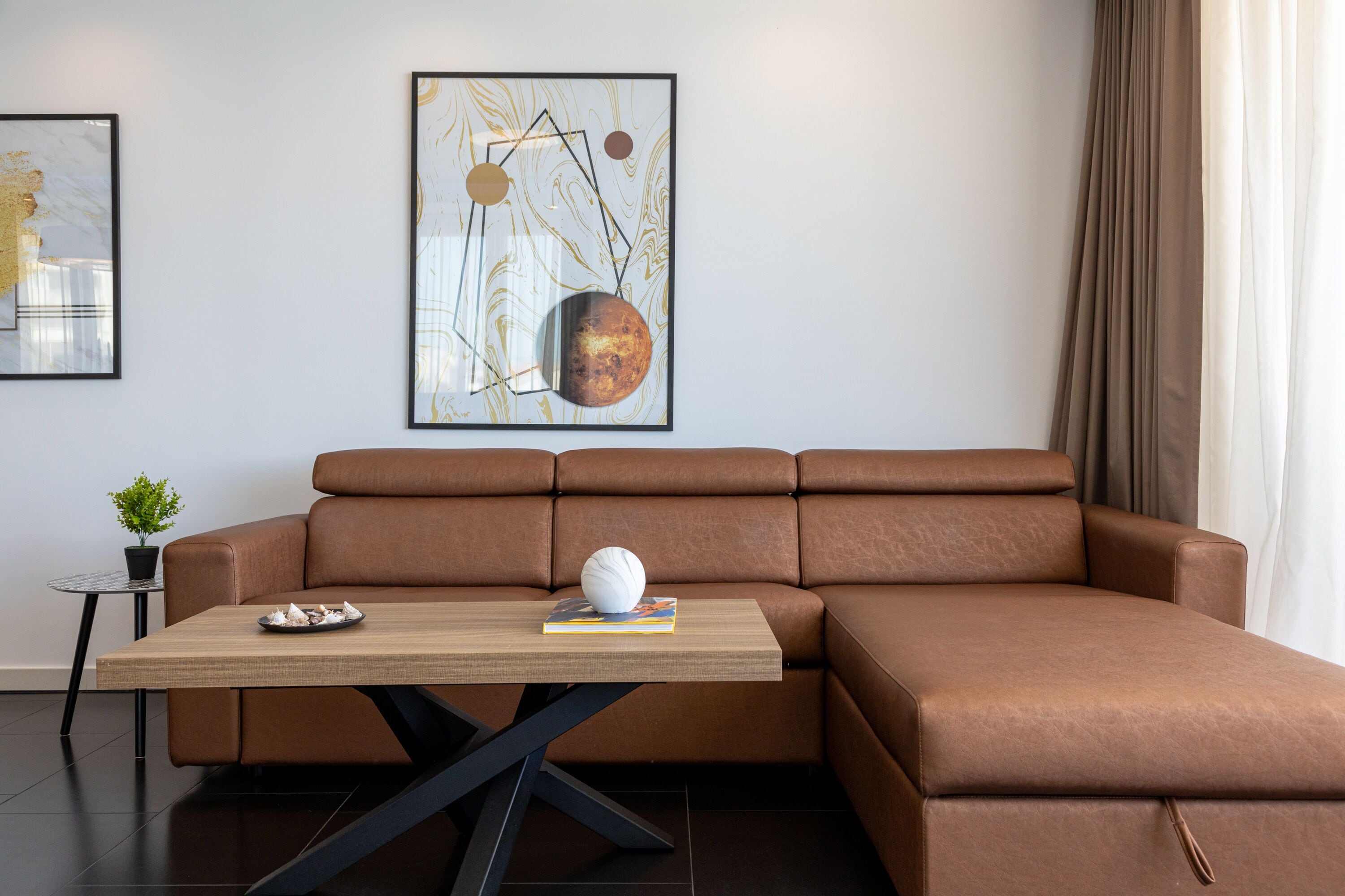 Un salon moderne avec un canapé en cuir marron, une table basse en bois et deux tableaux abstraits encadrés accrochés au mur.