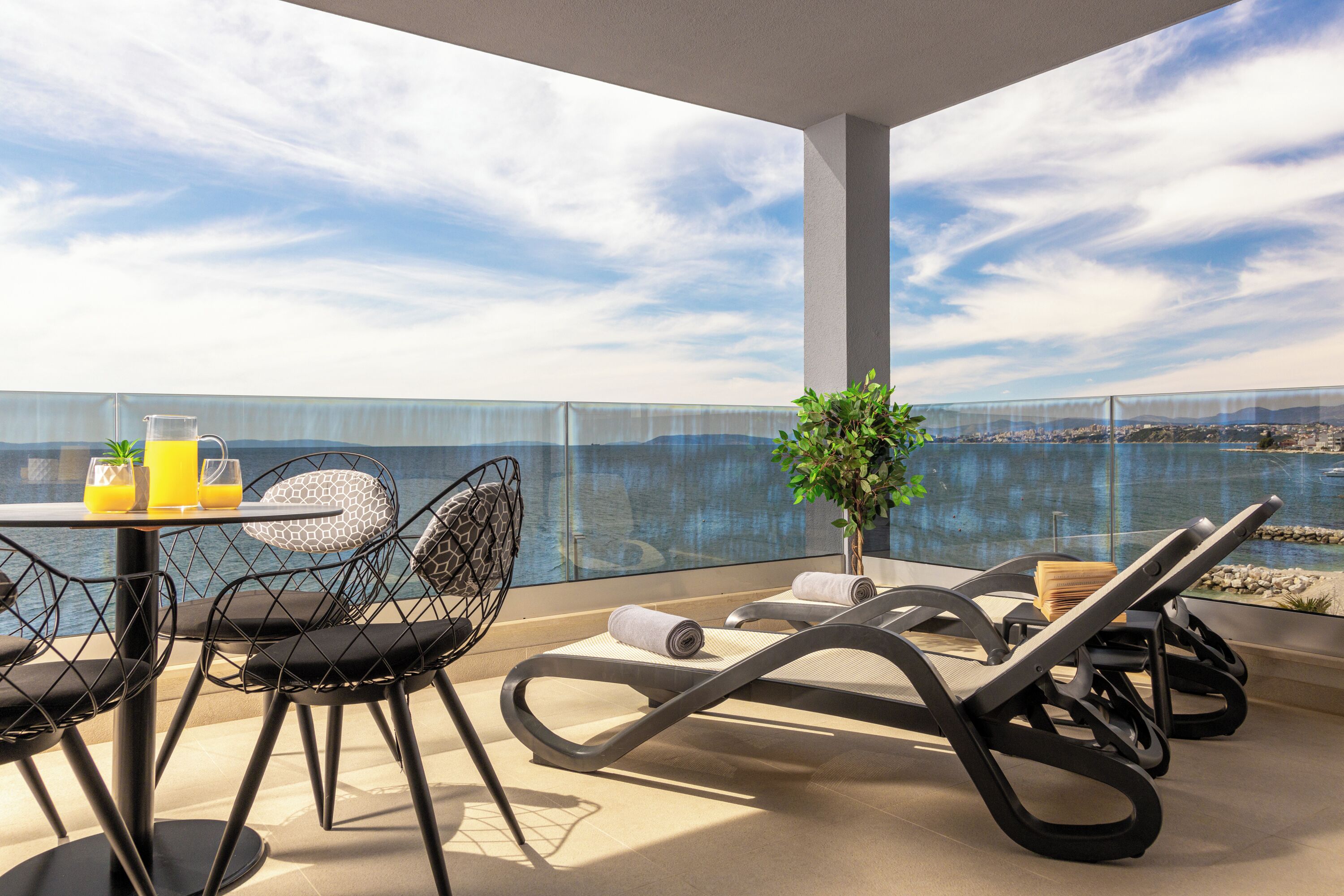 Ein Balkon mit Tisch, Stühlen, einer Pflanze und Blick auf das Wasser.