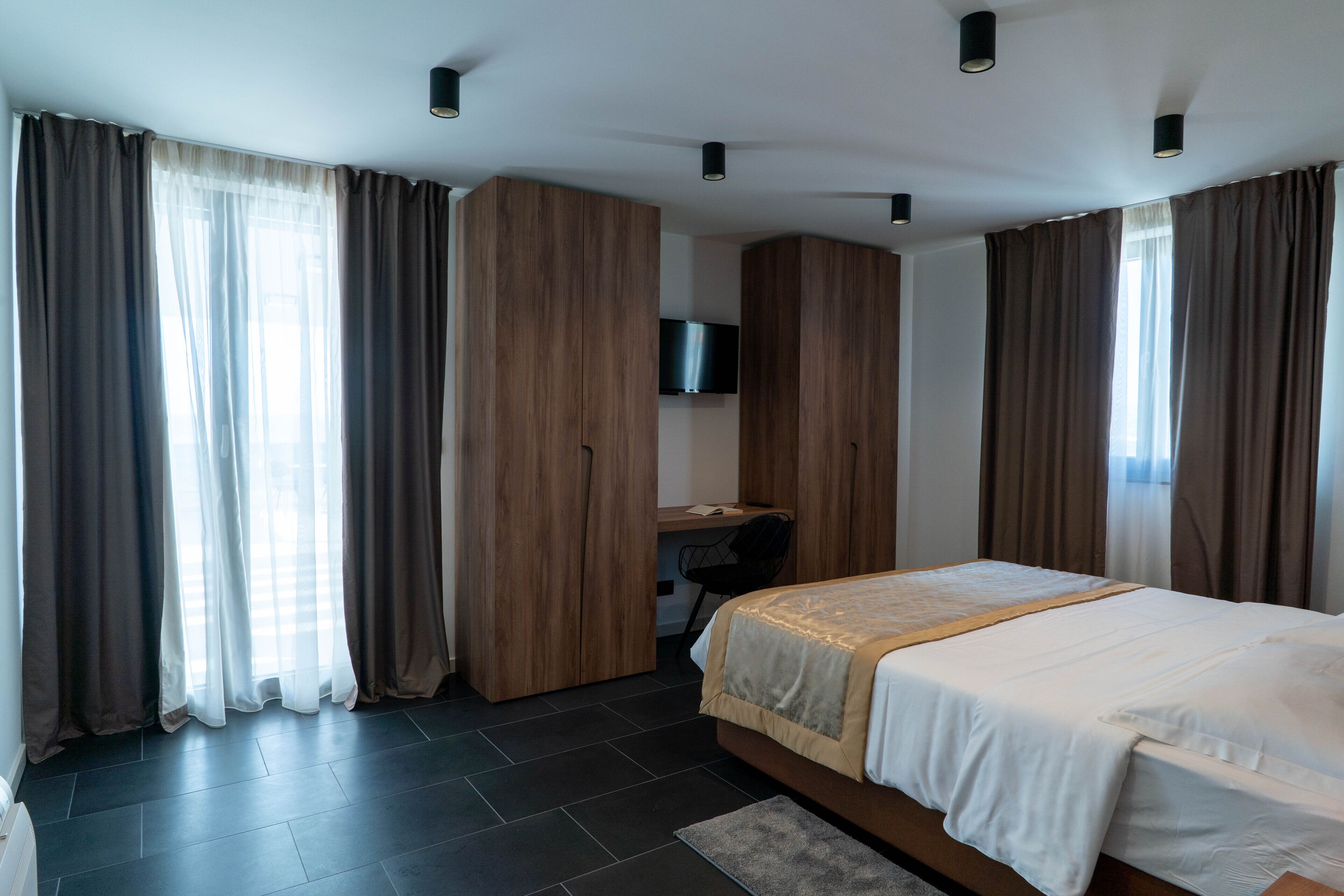 A modern bedroom with a large bed, dark flooring, and wooden wardrobe.