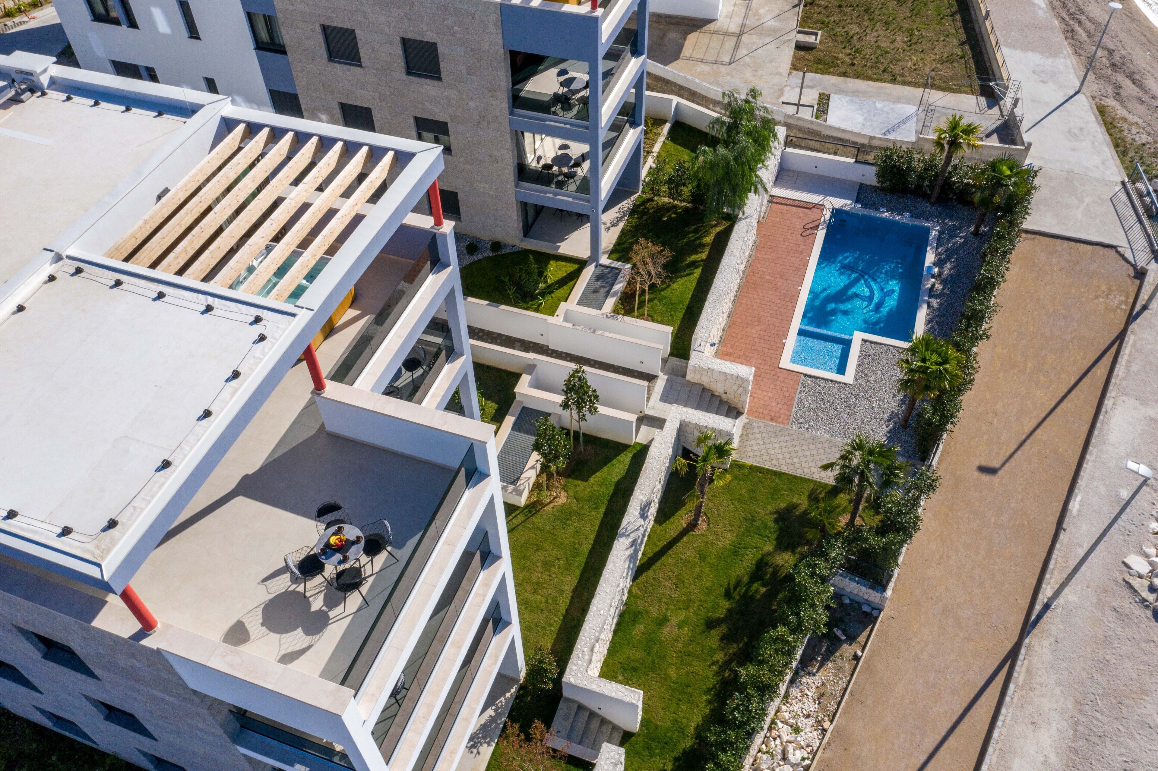 A modern building with a rooftop terrace, a swimming pool, and a landscaped garden.