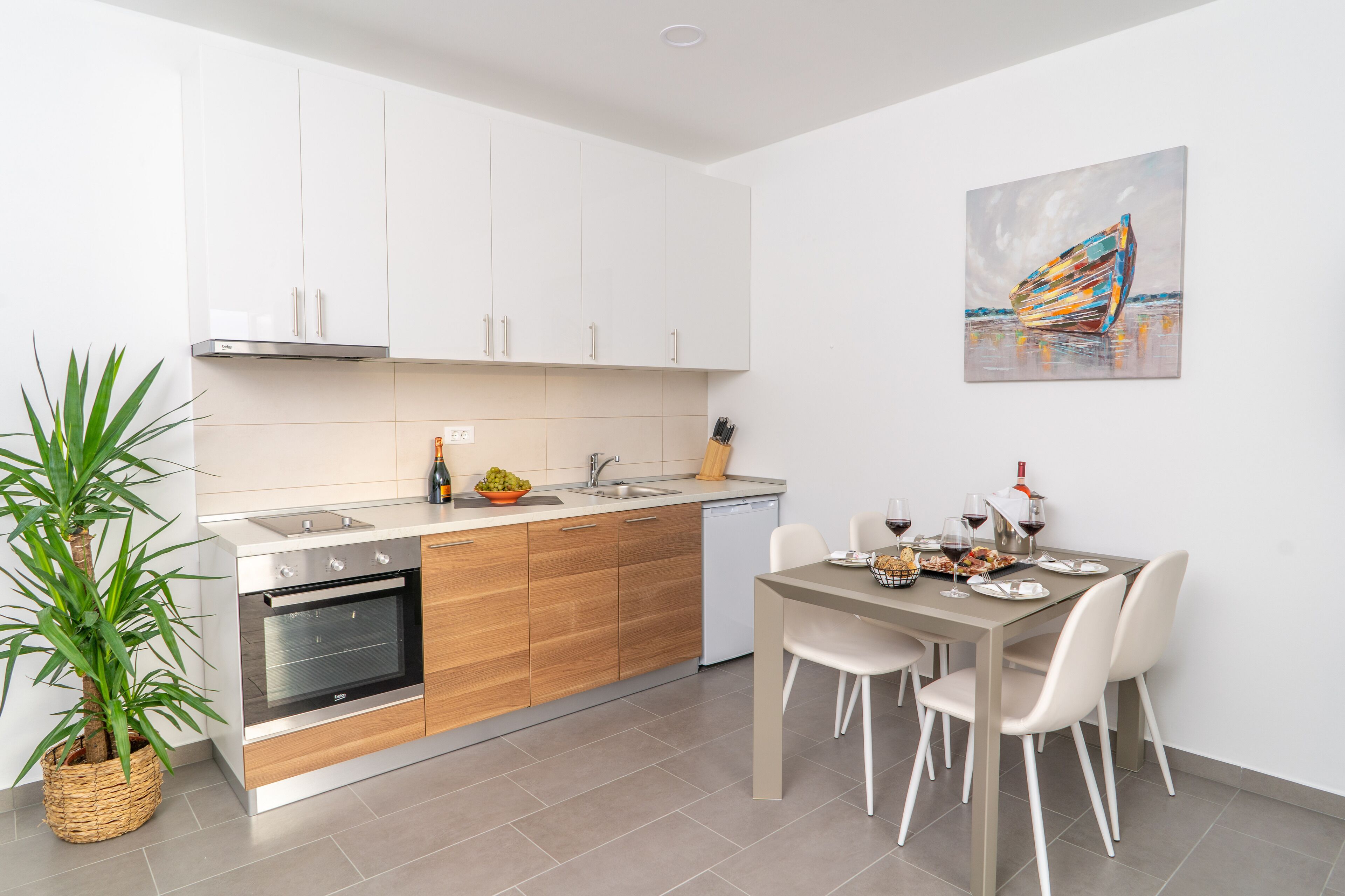 Una cocina moderna con armarios blancos, horno empotrado y comedor con mesa y sillas.