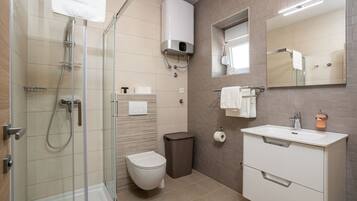 A modern bathroom with a glass shower enclosure, a toilet, a sink with a mirror, and a towel rack.