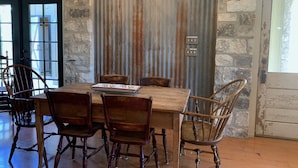 A rustic dining area with a wooden table and chairs, a chandelier, and a stone wall. - Dog-Trot Home on secluded acreage with pool and game room. (Spring Branch)