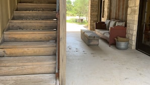 A wooden staircase leading to a stone-walled porch with a cushioned seating area and a metal bucket. - Dog-Trot Home on secluded acreage with pool and game room. (Spring Branch)