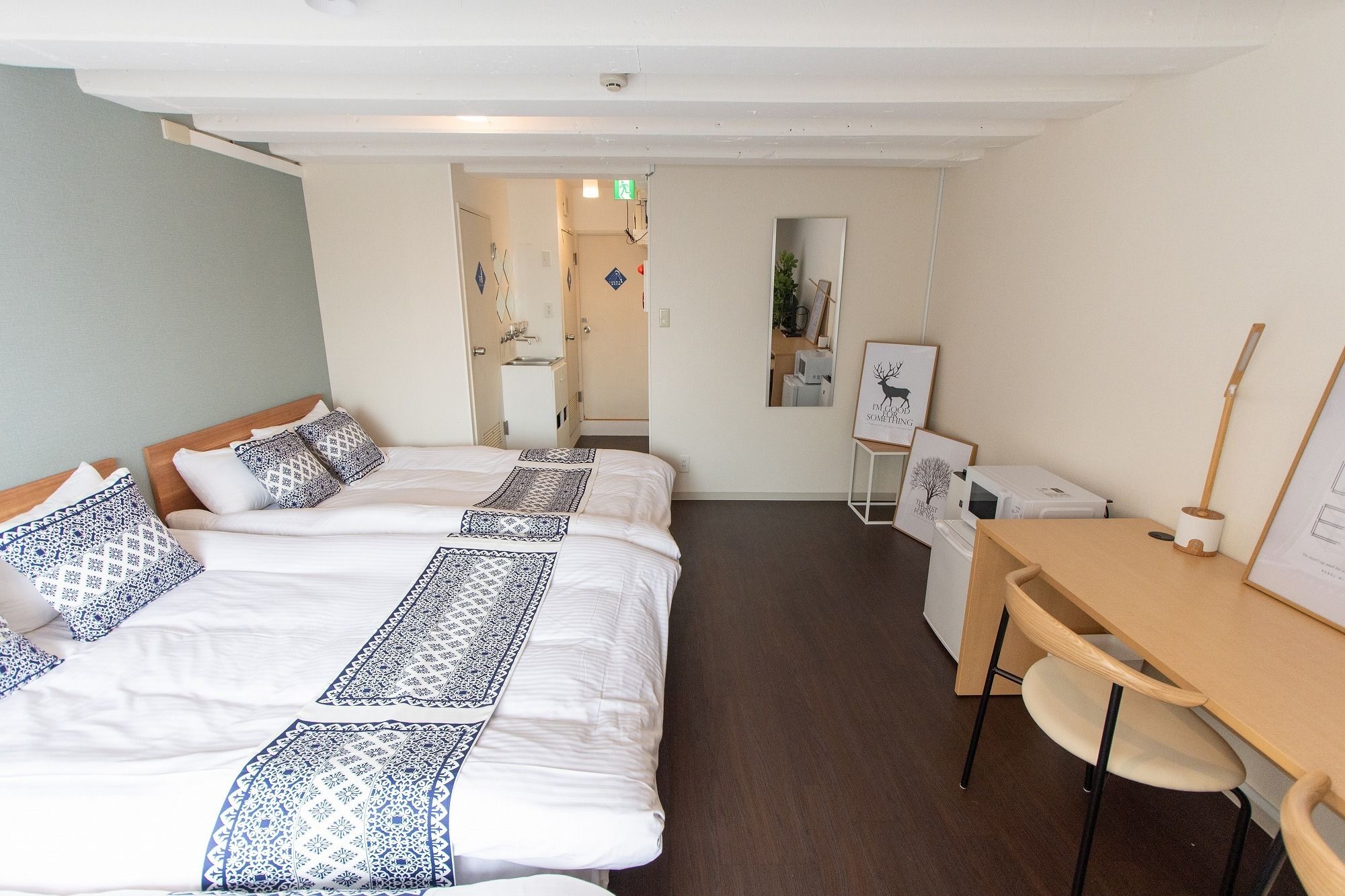 Una habitación de hotel con dos camas, un escritorio, una silla, un espejo y una pequeña cocina.