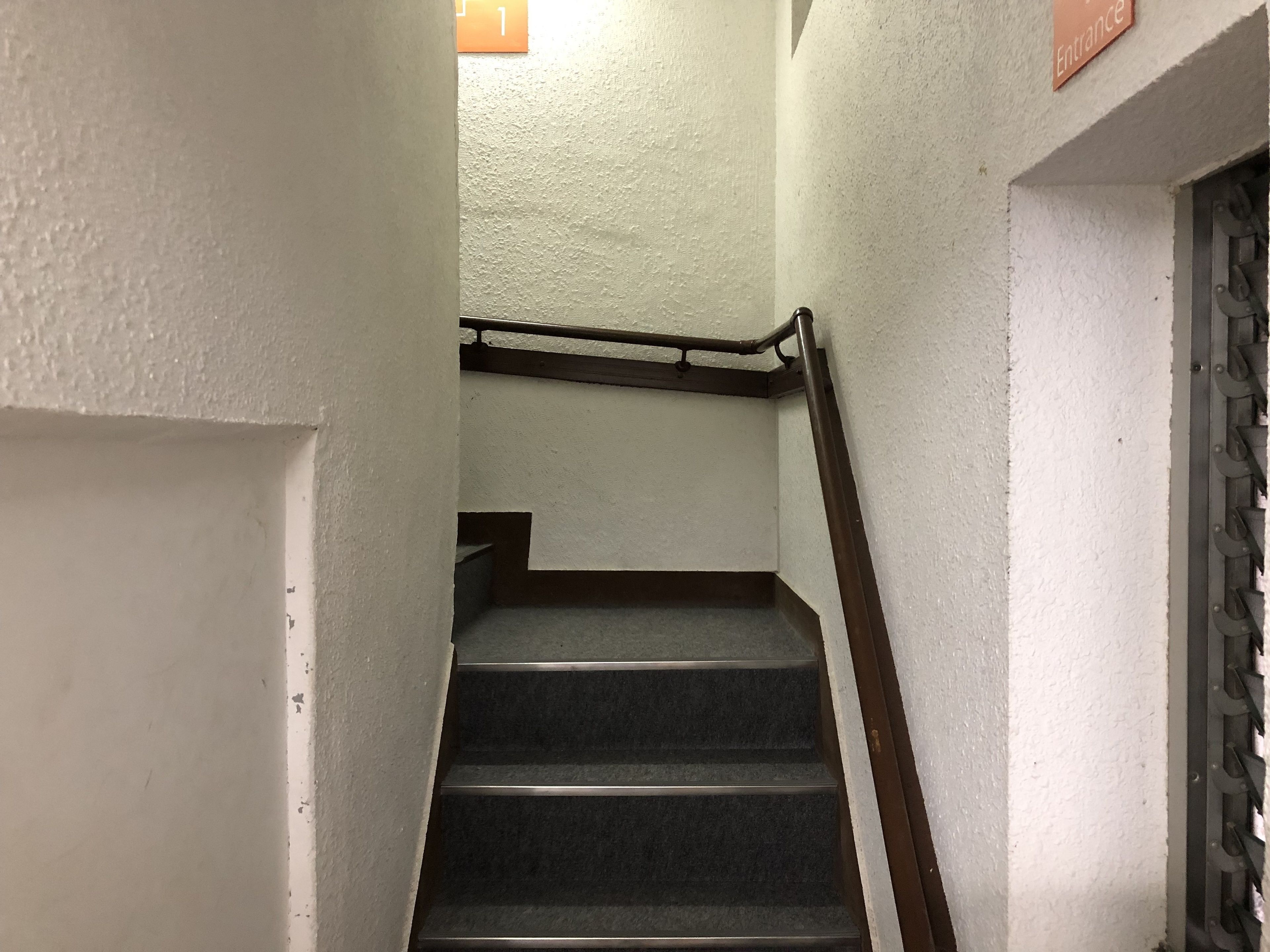 Una escalera con barandilla y una puerta con celosía metálica.