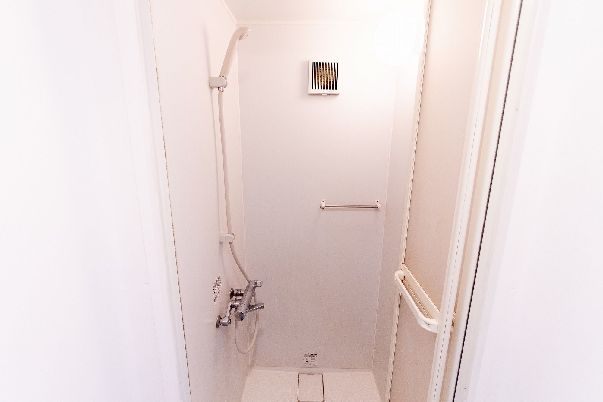 Un petit espace de douche fermé, de couleur blanche, équipé d’un pommeau de douche à main, d’un radiateur mural et d’une barre à serviettes.