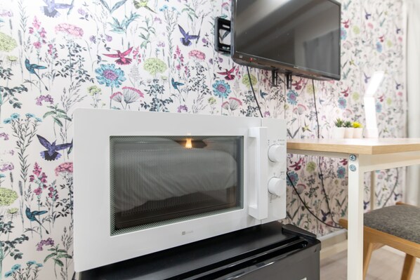 Un microondas sobre un soporte portátil, un televisor montado en la pared y un estampado de flores en el papel tapiz.