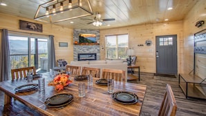A wooden cabin interior with a dining area, kitchen, and a fireplace.