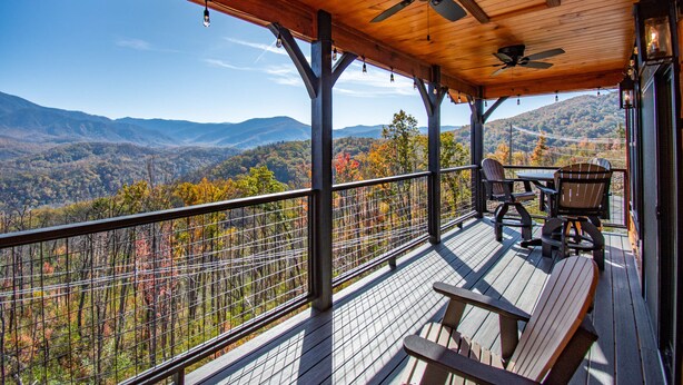 A wooden deck with a table and chairs, overlooking a mountainous landscape.