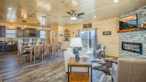 A spacious living area with a fireplace, wooden ceiling, and a dining area with a table and chairs.