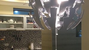 Et moderne køkken med spiseplads, der fremviser et unikt, kugleformet lysarmatur, et glasbord og en grå sofa.