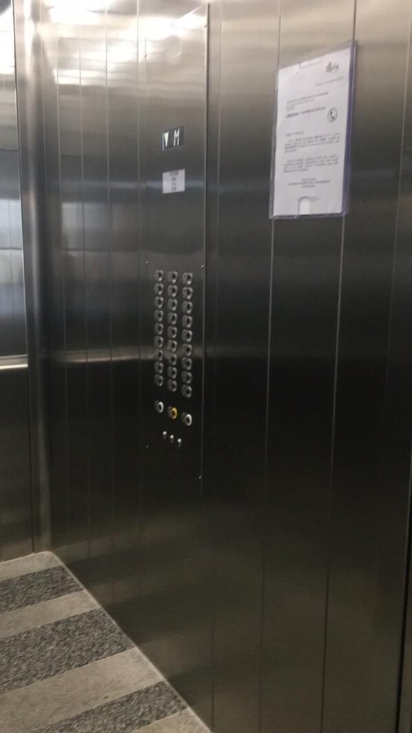 An elevator interior with a control panel, emergency stop button, and a notice.