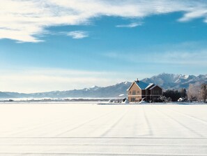 A large, two-story house with a snow-covered roof, situated in a snowy landscape with mountains in the background. - Shooting Star the Bed & Breakfast (Nakafurano)