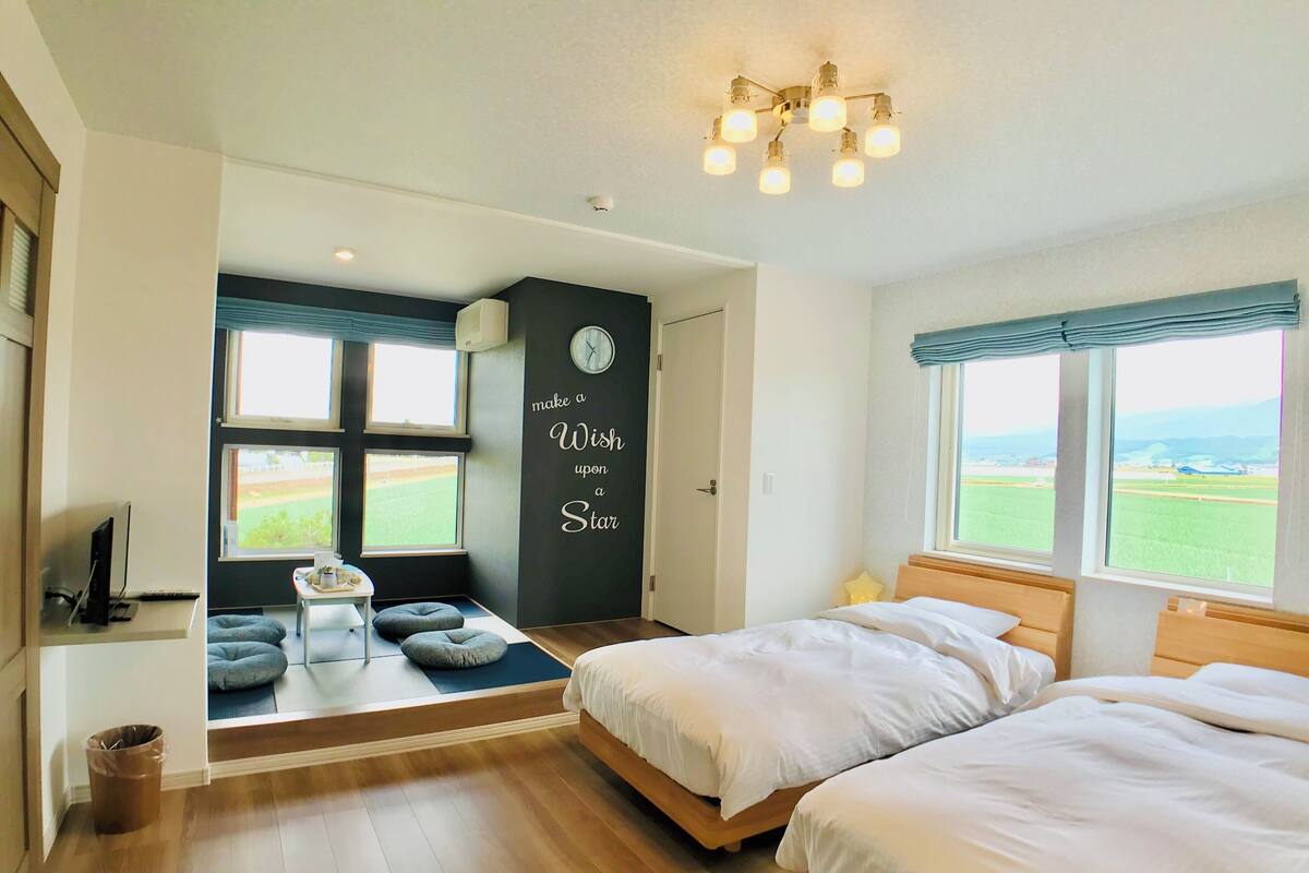 Un dormitorio con dos camas, un escritorio y una ventana con vistas a un campo.
