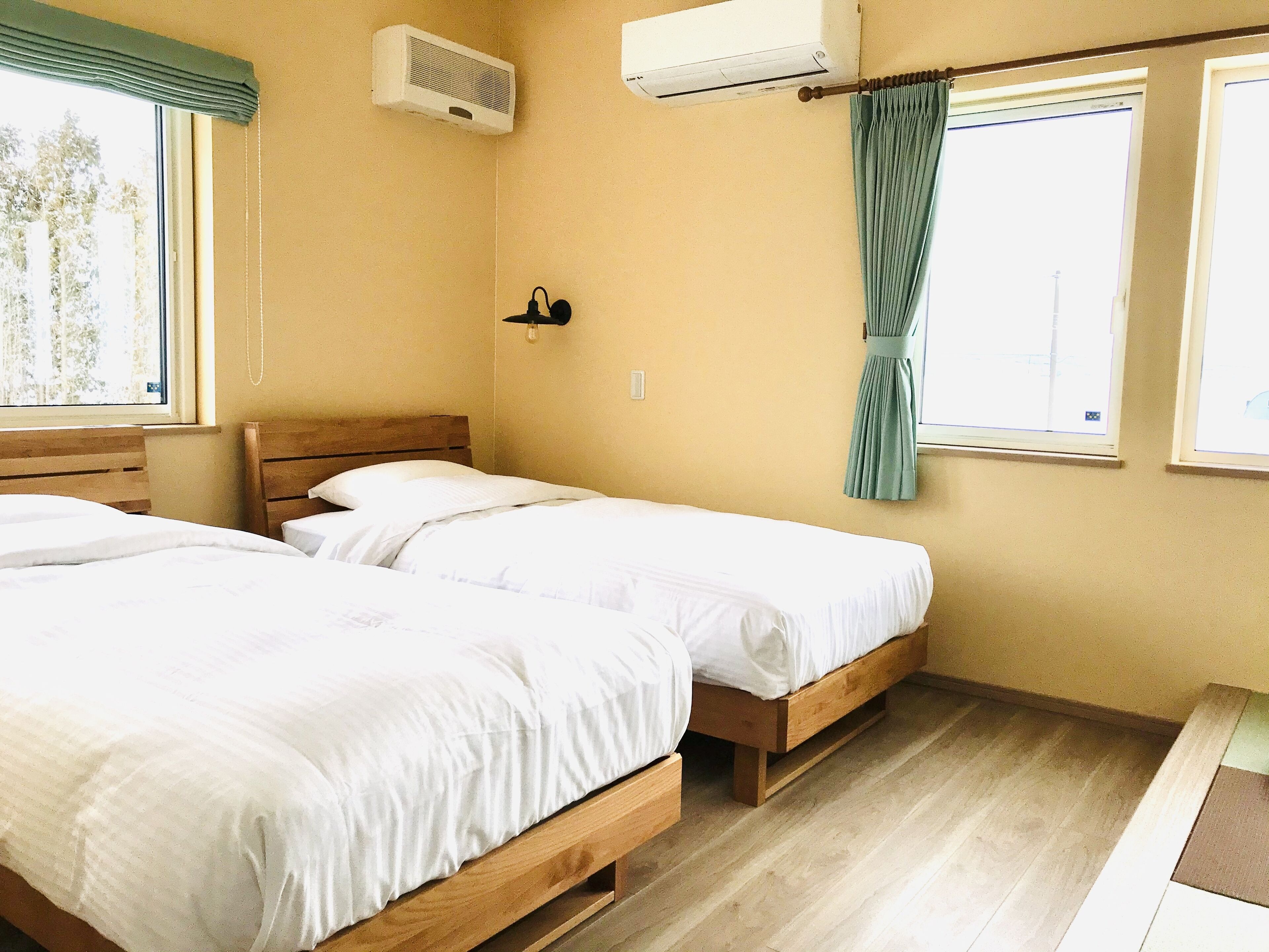 Una habitación con dos camas de madera, un ventanal con cortina y un equipo de aire acondicionado.