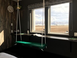 A room with a wooden wall, a clock, a window with a view of a field, and a green bench. - Shooting Star the Bed & Breakfast (Nakafurano)