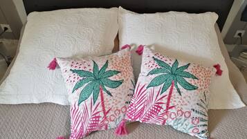 Een bed met twee witte kussens en twee sierkussens met een palmboom- en hartmotief.