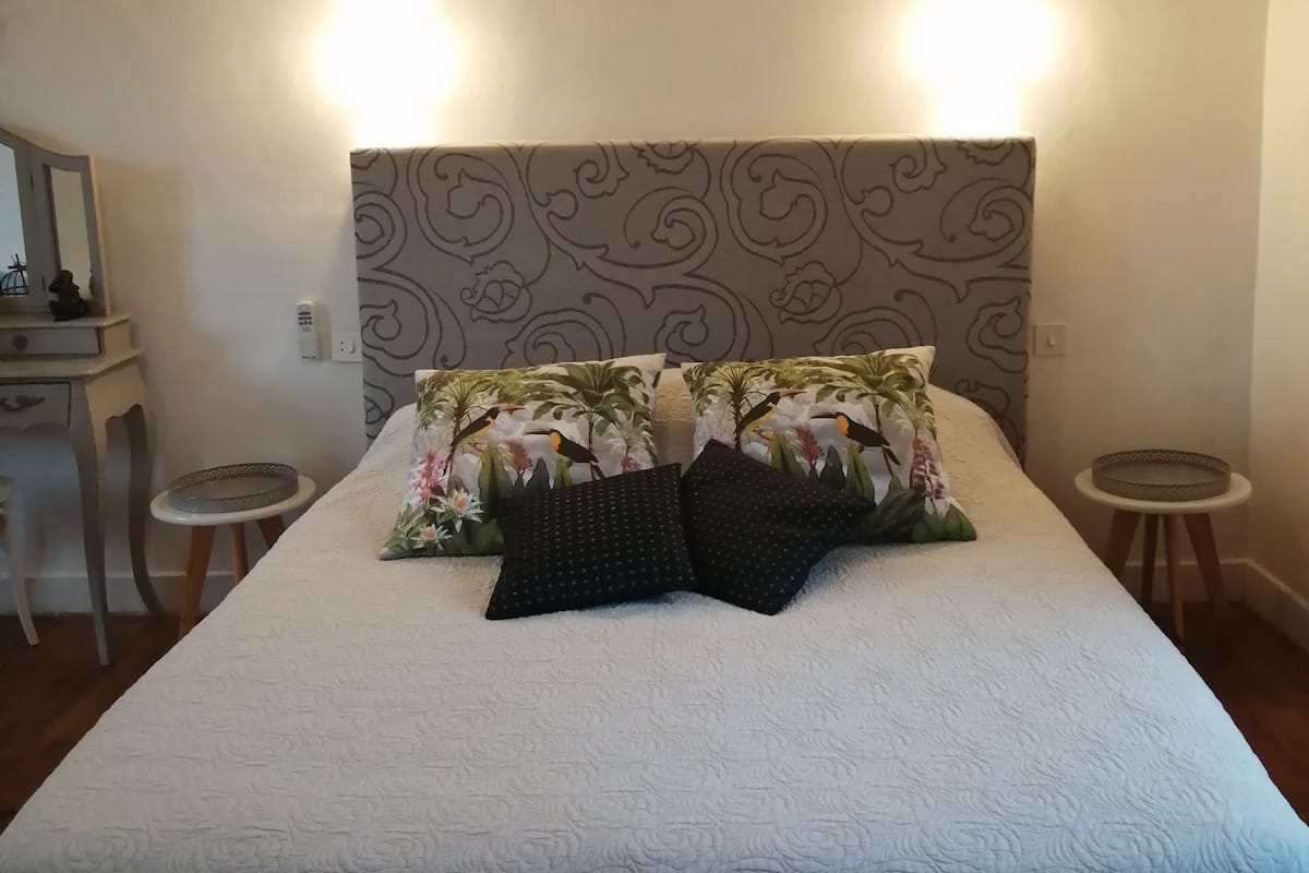 Ein ordentlich bezogenes Bett mit einem blumengemusterten Kopfteil, zwei Nachttischen und einem an der Wand hängenden Kunstwerk darüber.