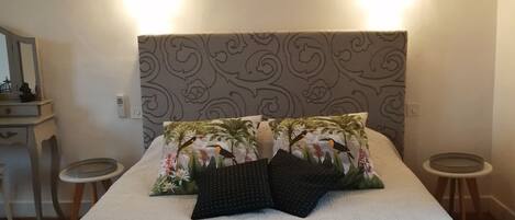 Una cama bien hecha con un cabecero estampado con motivos florales, dos mesitas de noche y una obra de arte colgada en la pared sobre la cama.