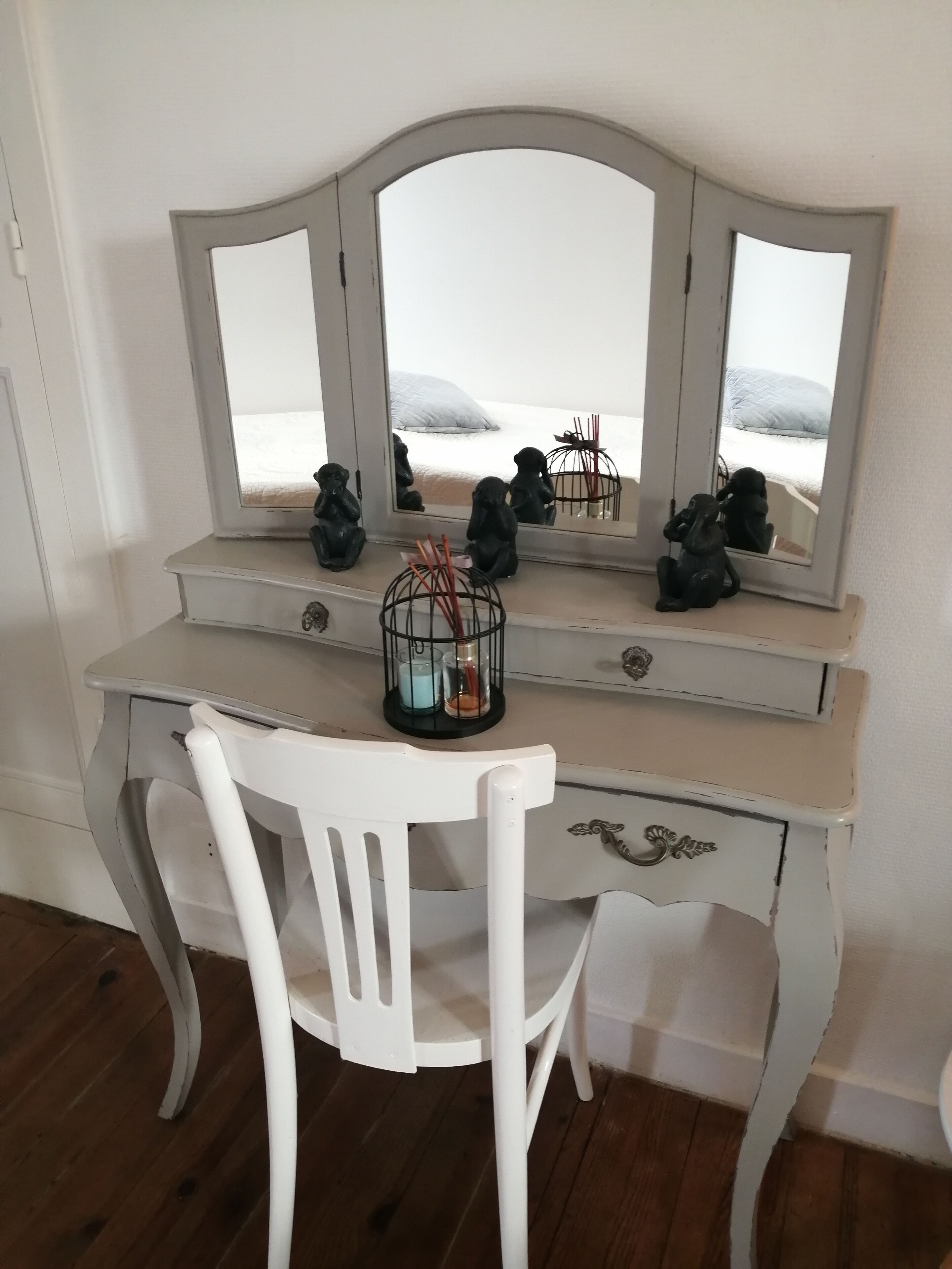 A white wooden desk with a mirror, two black figurines, and a candle holder.