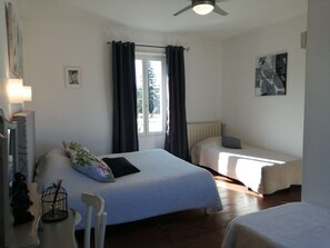 A bedroom with a large bed, a smaller bed, a chair, a window with curtains, and artwork on the wall. - Le Kouloury (Meyronne)