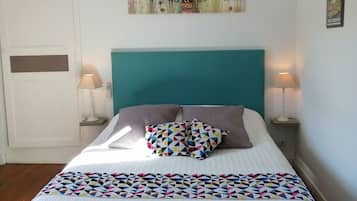 Un lit avec une tête de lit de couleur turquoise, deux lampes de chevet, une couverture à motifs géométriques colorés et un élément décoratif mural au-dessus du lit.