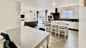 A modern kitchen with white cabinets, a black countertop, and a built-in oven. There is a dining area with a table and chairs, and a green sofa. - VillasHomeClet - Villa Les Alizés ⭐️ Terrace ⭐️ Beach ⭐️ A/C ⭐️ 3 bedrooms (VENSAC)