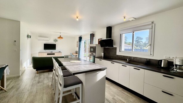 A modern kitchen with a large island, white cabinetry, and a window providing natural light. - VillasHomeClet - Villa Les Alizés ⭐️ Terrace ⭐️ Beach ⭐️ A/C ⭐️ 3 bedrooms (VENSAC)