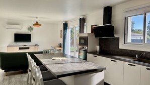 A modern kitchen with a central island, built-in appliances, and a dining area with a sofa and chairs. - VillasHomeClet - Villa Les Alizés ⭐️ Terrace ⭐️ Beach ⭐️ A/C ⭐️ 3 bedrooms (VENSAC)