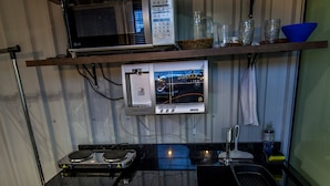 Cocina compacta con microondas, estufa y refrigerador. Hay repisas sobre la encimera con diversos utensilios de cocina.