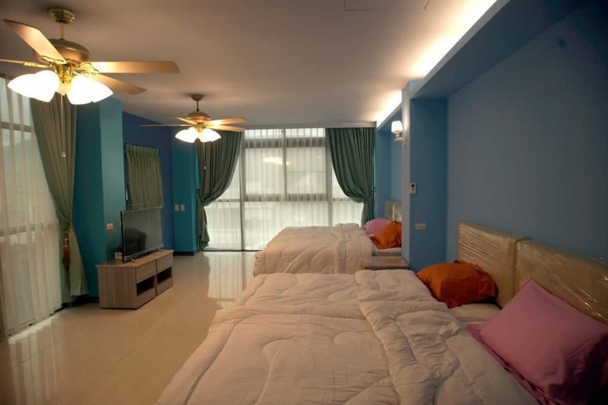 Ein Hotelzimmer mit zwei Betten, einem Fernseher, Deckenventilatoren und großen Fenstern mit Vorhängen.