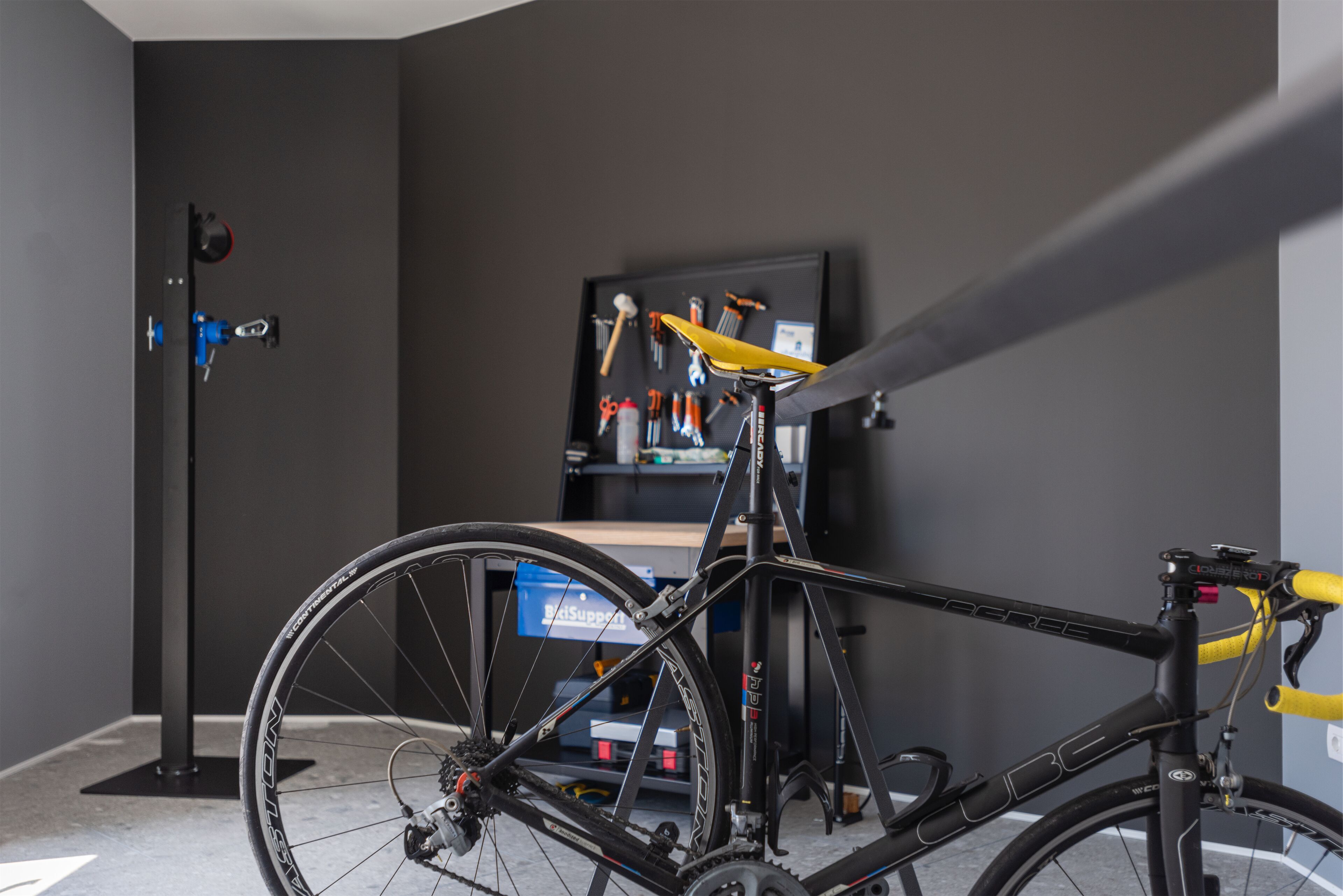 A bicycle in a room with a tool rack and a blue storage unit.