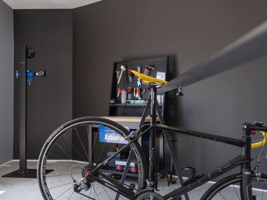 A bicycle in a room with a tool rack and a blue storage unit.
