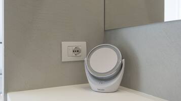 A modern bathroom with a white sink, a wall-mounted outlet, and a white, circular, contemporary mirror.
