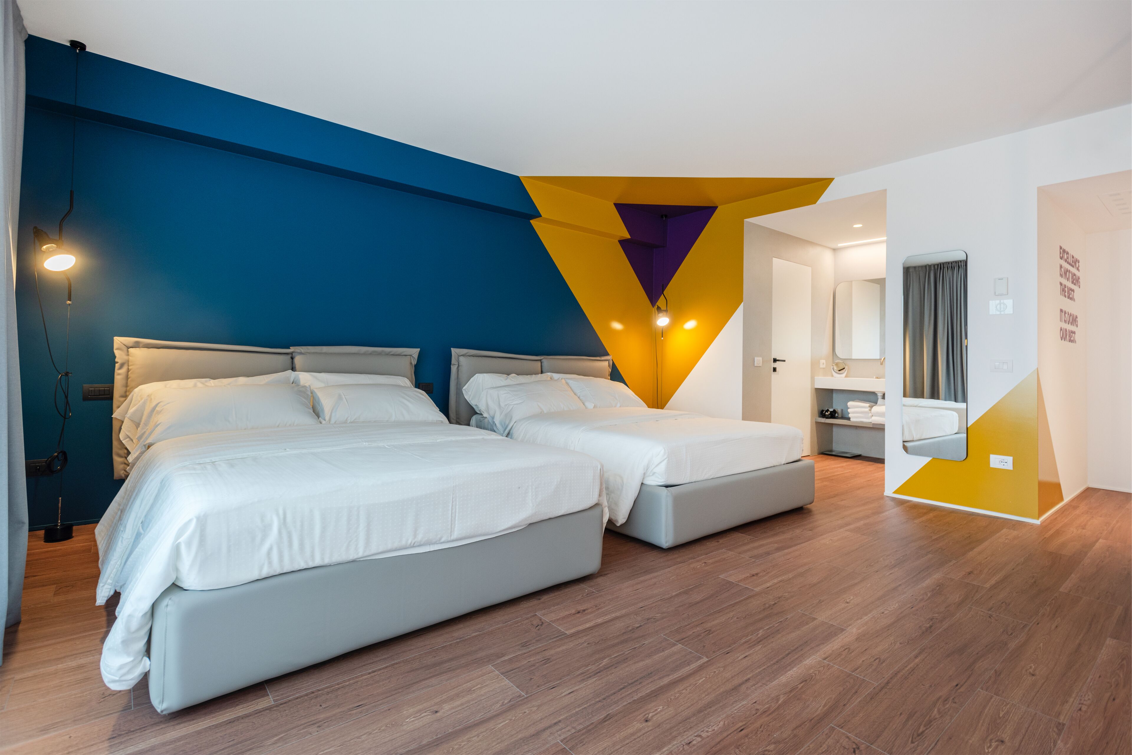 A modern hotel room with two beds, a large mirror, and a geometric wall design.