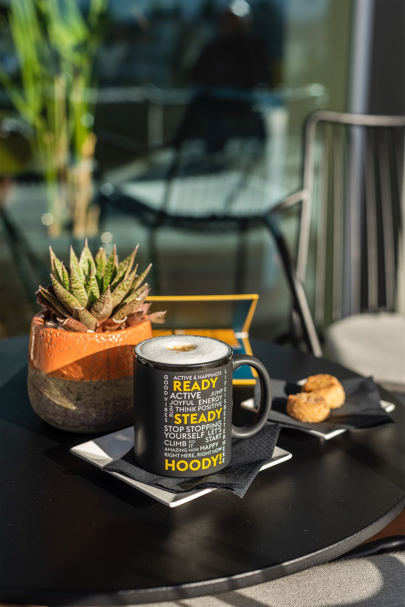 Una mesa con un suculento en maceta, una taza con palabras motivacionales y un plato con galletas.