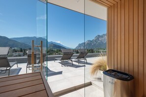 A balcony with a glass wall, outdoor seating, and a view of mountains. - Hoody Active & Happiness Hotel (Arco)