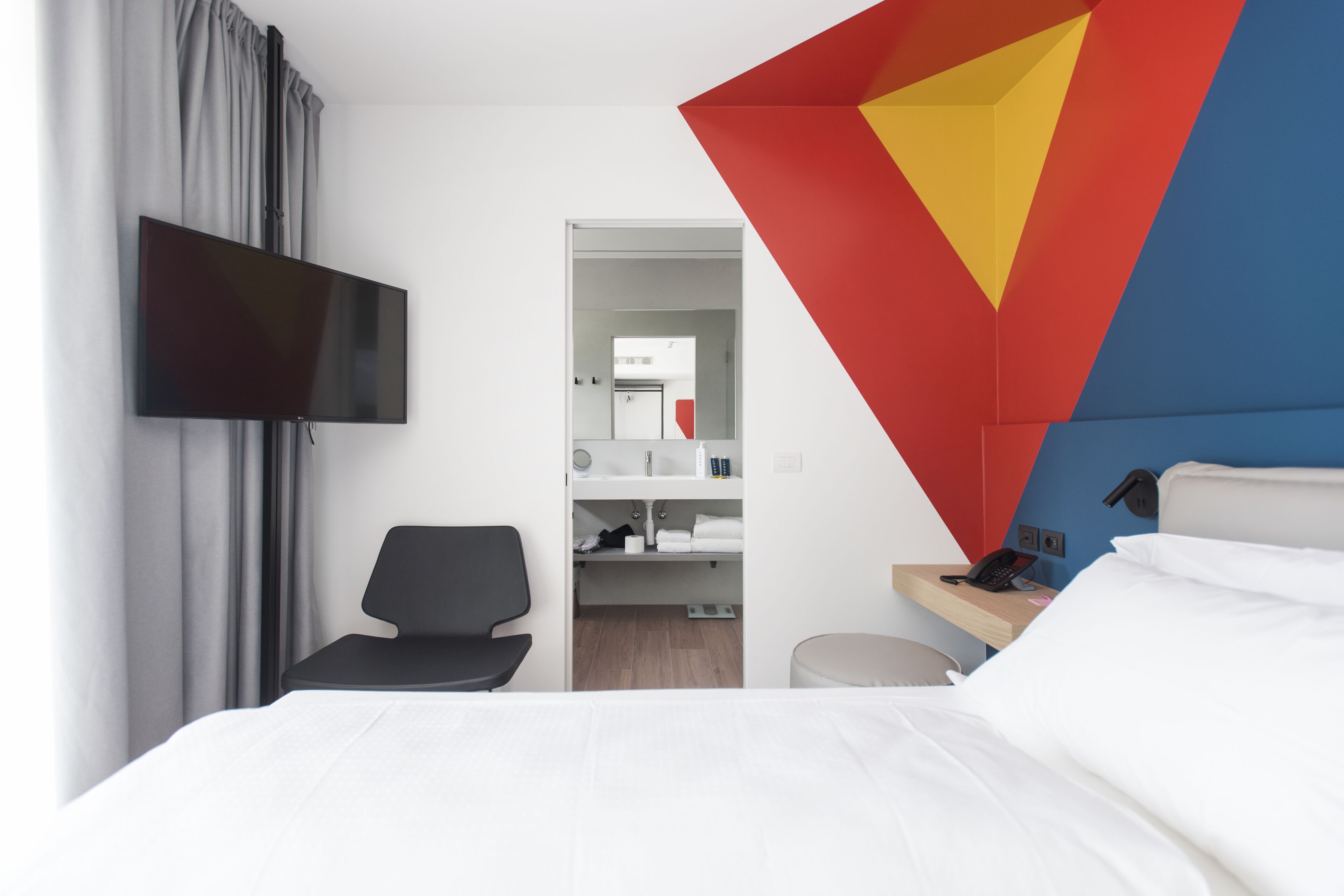 Una habitación de hotel moderna con televisión de pantalla plana, escritorio con teléfono, una silla y una cama.