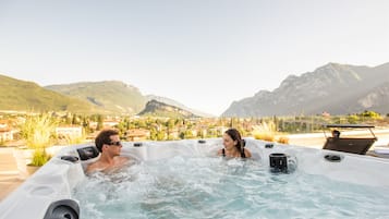 A hot tub with two people, surrounded by mountains and a residential area.